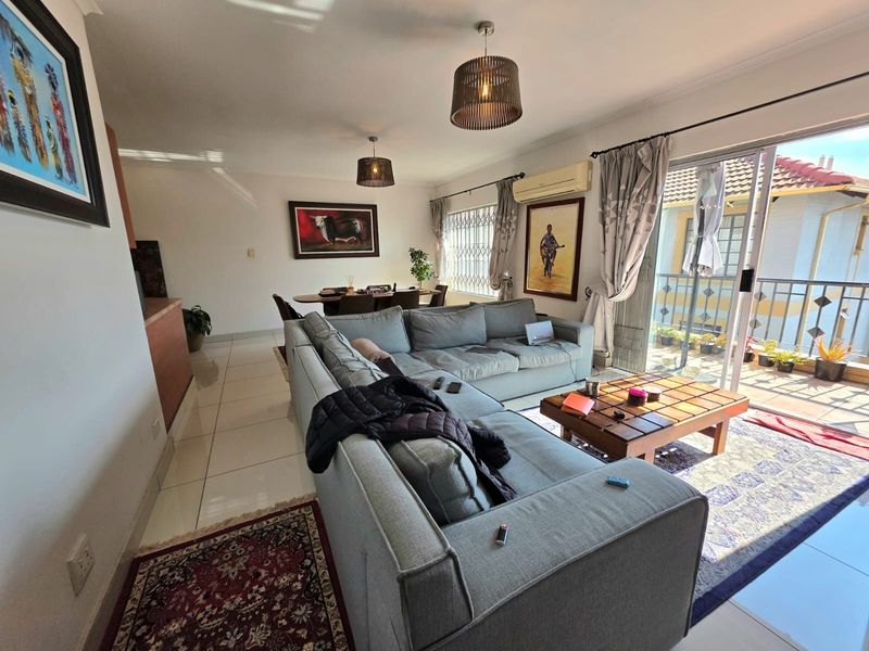Spacious open-plan living and dining area featuring tiled floors, modern pendant lighting, and direct access to a private balcony through sliding glass doors.
