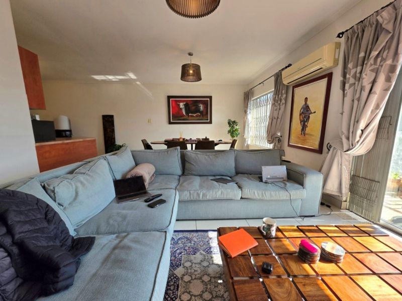 Open-plan living and dining area featuring tiled floors, a wall-mounted air conditioning unit, and direct access to an outdoor balcony through sliding glass doors.
