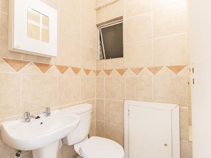 A compact bathroom featuring tiled walls, a pedestal basin, and a standard toilet, offering a functional layout ready for modern updates.