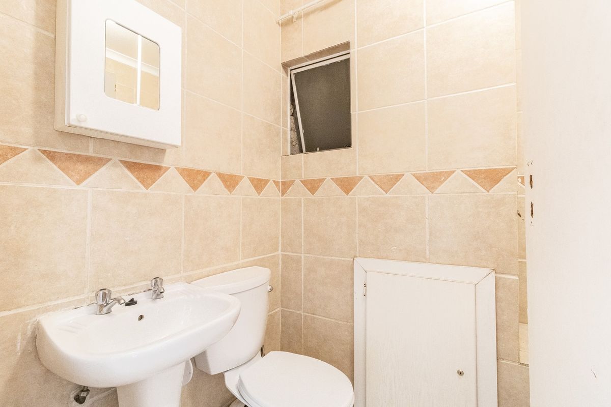 A compact bathroom featuring tiled walls, a pedestal basin, and a standard toilet, offering a functional layout ready for modern updates.