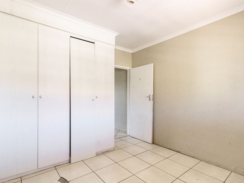 An empty bedroom featuring built-in cupboards, tiled flooring, and neutral wall finishes, ready for personalization.