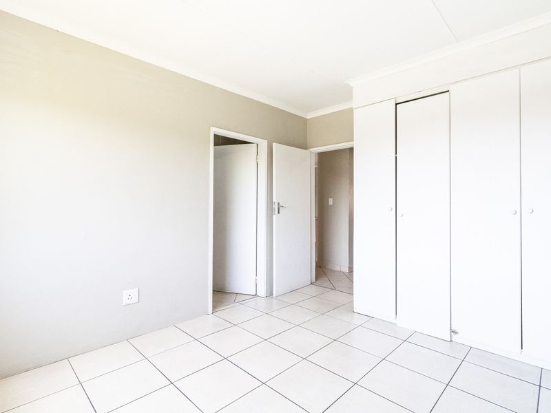 A bright, empty bedroom featuring neutral walls, white tiled flooring, and built-in cupboards, offering a clean and versatile space.
