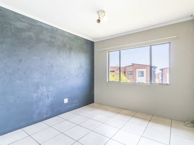 A bright, empty bedroom featuring tiled flooring, a large window with an aluminium frame, and a feature wall with a textured finish.