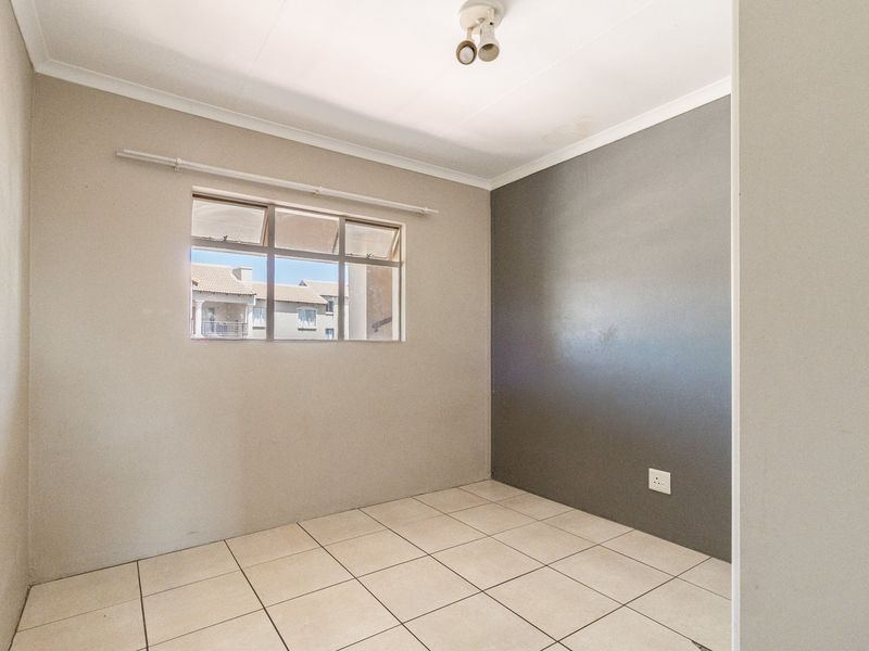An empty bedroom featuring tiled flooring, a window with a curtain rail, and a neutral color scheme with a grey accent wall.