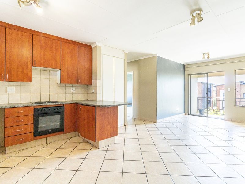 Open-plan kitchen and living area featuring wooden cabinetry, built-in oven, tiled flooring, and direct access to a balcony through sliding glass doors.