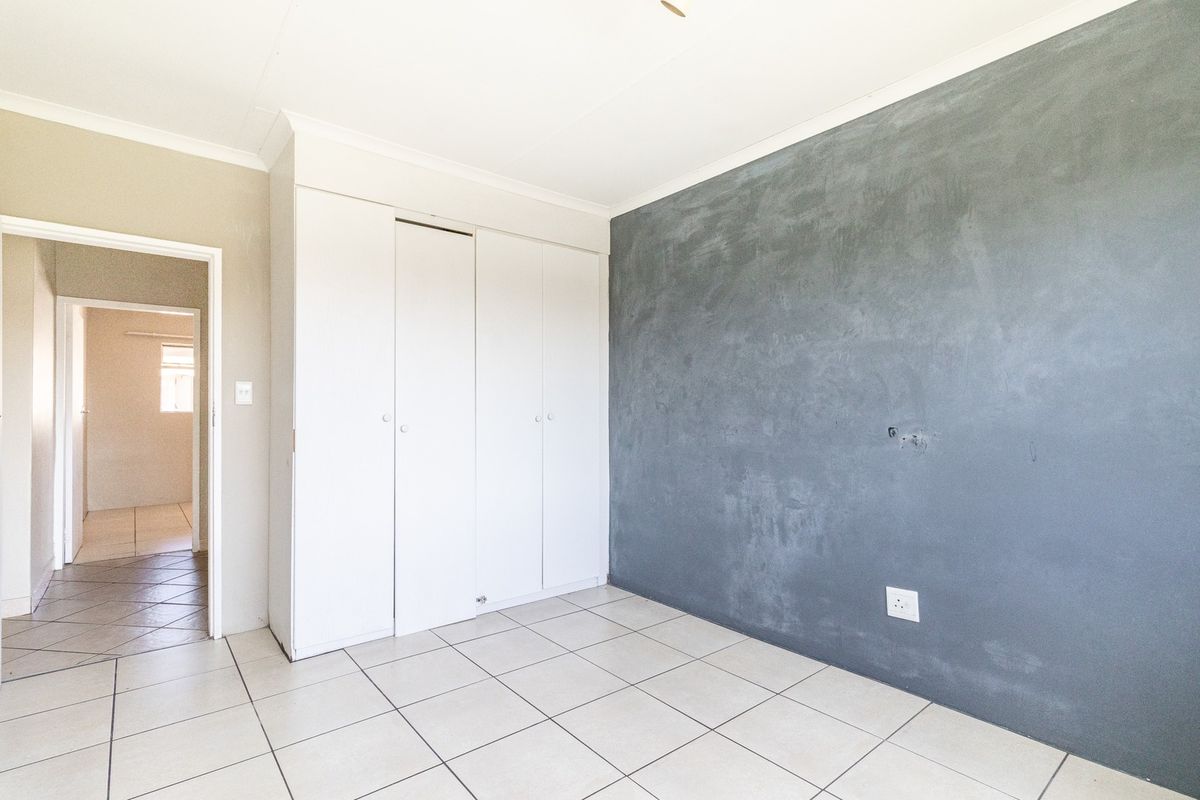 An empty bedroom featuring tiled flooring, built-in cupboards, and a feature wall with a textured grey finish.