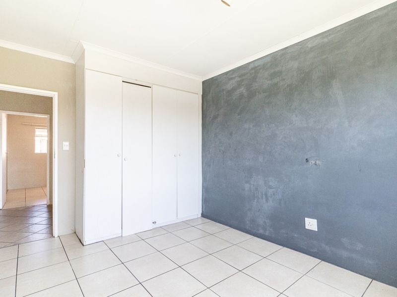 An empty bedroom featuring tiled flooring, built-in cupboards, and a feature wall with a textured grey finish.