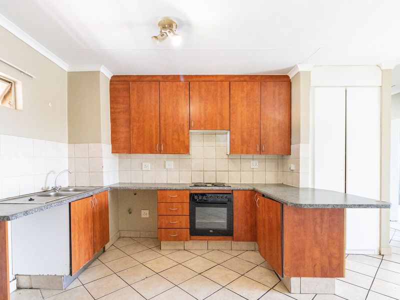 A functional kitchen featuring wooden cabinetry, laminate countertops, a built-in oven, hob, and tiled flooring, offering a clean and practical workspace.
