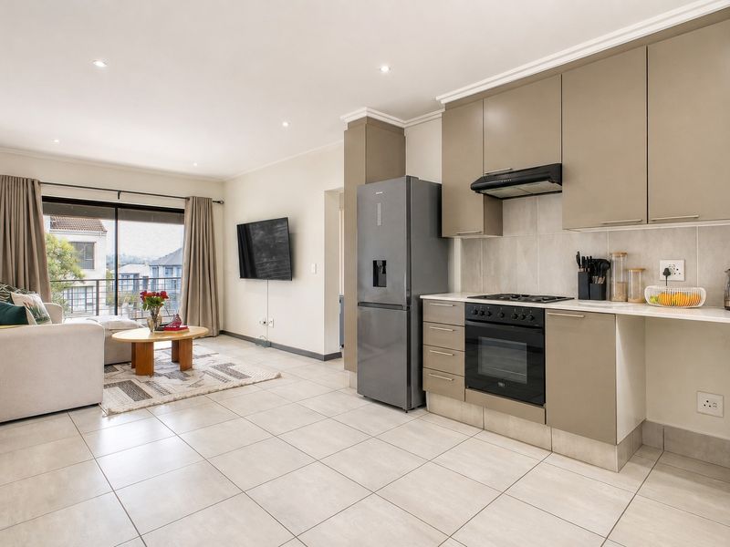 Modern open-plan living area featuring a well-appointed kitchen with built-in cabinetry, gas hob, and tiled flooring, leading to a private balcony.