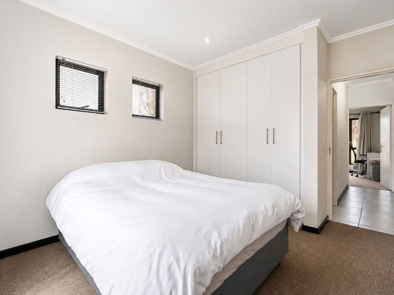 A well-maintained bedroom featuring neutral walls, built-in cupboards, carpeted flooring, and recessed downlights, offering a clean and functional living space.