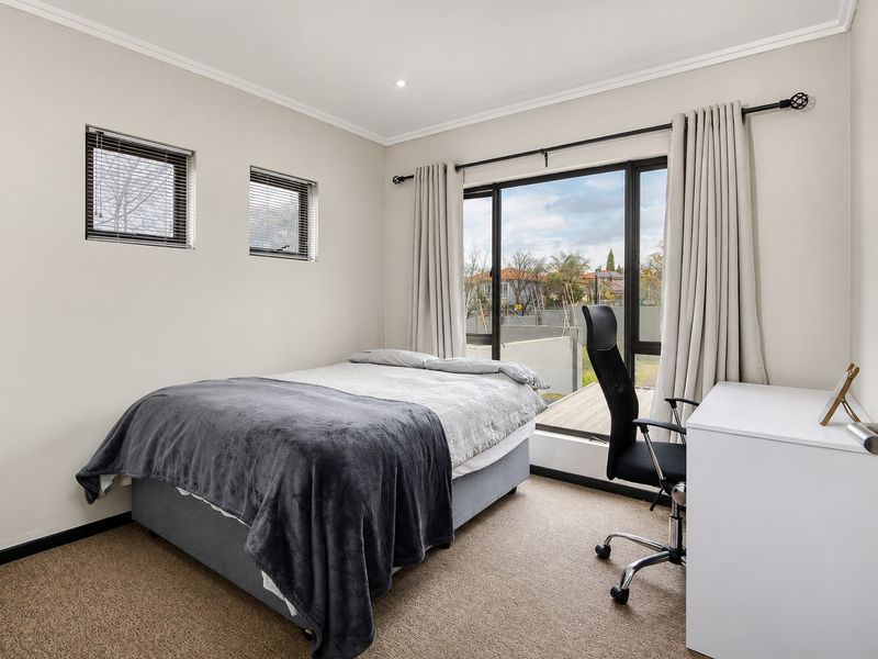 A well-lit bedroom featuring neutral walls, carpet flooring, recessed downlights, and a sliding glass door providing access to an outdoor area.