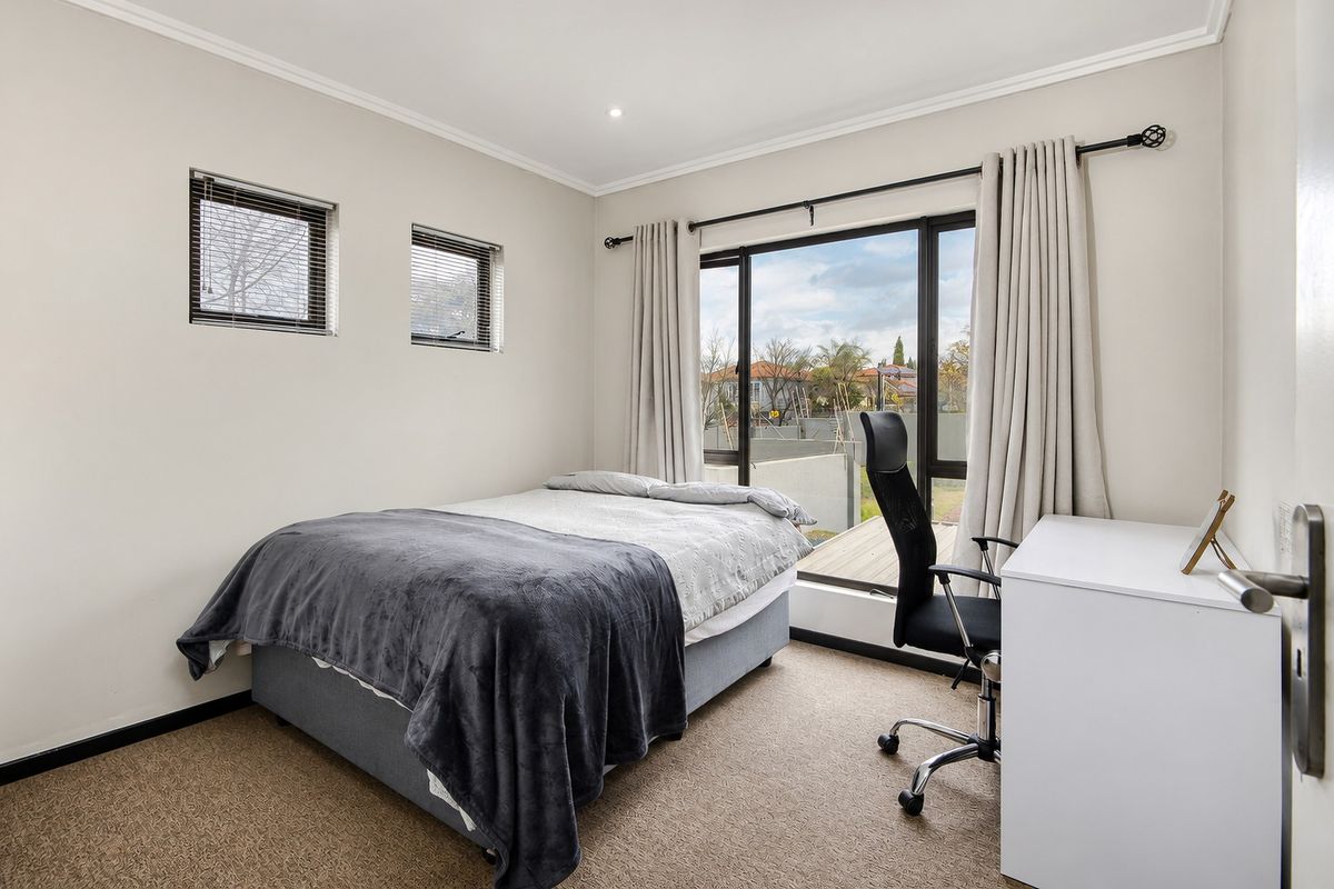A well-lit bedroom featuring neutral walls, carpet flooring, recessed downlights, and a sliding glass door providing access to an outdoor area.