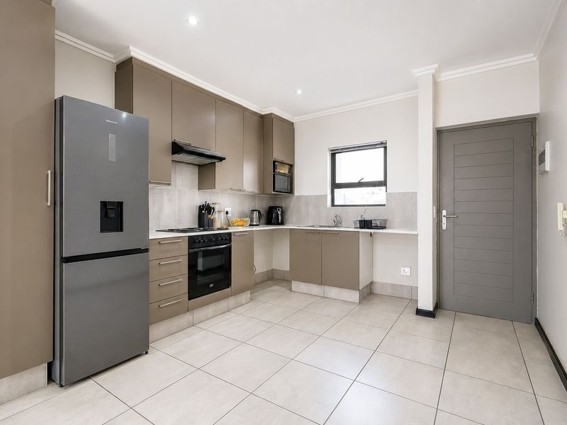 Modern kitchen featuring sleek taupe cabinetry, built-in oven and hob, tiled backsplash, and neutral floor tiles, offering a clean and functional cooking space.
