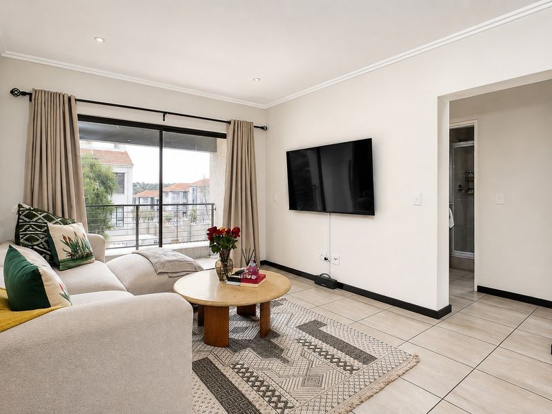 A bright, well-maintained living room featuring tiled floors, recessed lighting, and direct access to a private balcony through large sliding glass doors.