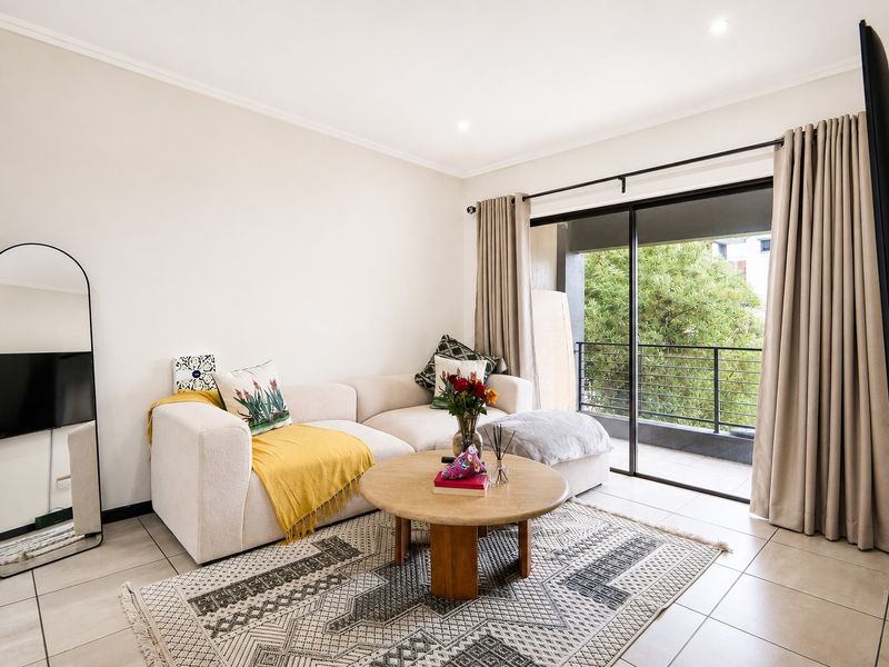 A bright and well-maintained living room featuring neutral tiled flooring, recessed lighting, and a large sliding glass door providing access to a balcony.