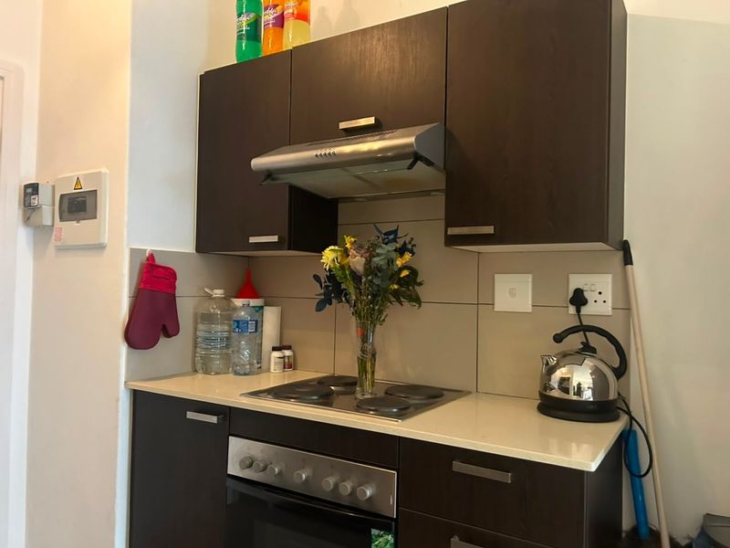 Compact kitchen featuring dark wood cabinetry, stone countertops, a built-in oven, and an extractor fan with a tiled splashback.