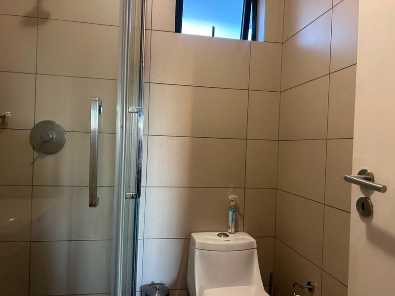 A functional bathroom featuring a glass-enclosed shower and a modern top-flush toilet with neutral wall tiling.