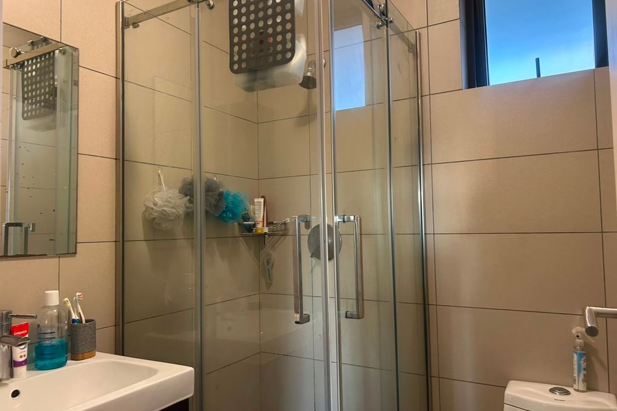 A functional bathroom featuring a glass shower enclosure, wall-mounted vanity basin, and neutral ceramic wall tiling.