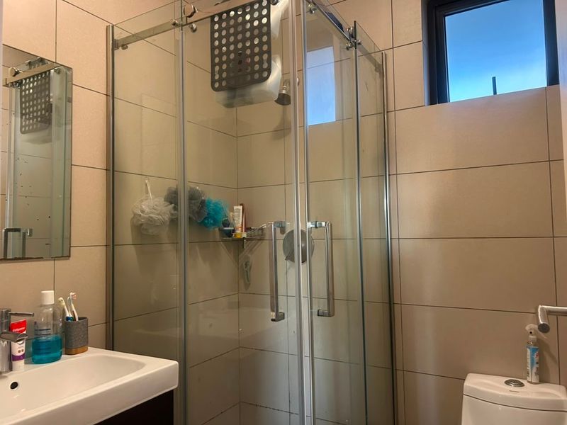 A functional bathroom featuring a glass shower enclosure, wall-mounted vanity basin, and neutral ceramic wall tiling.