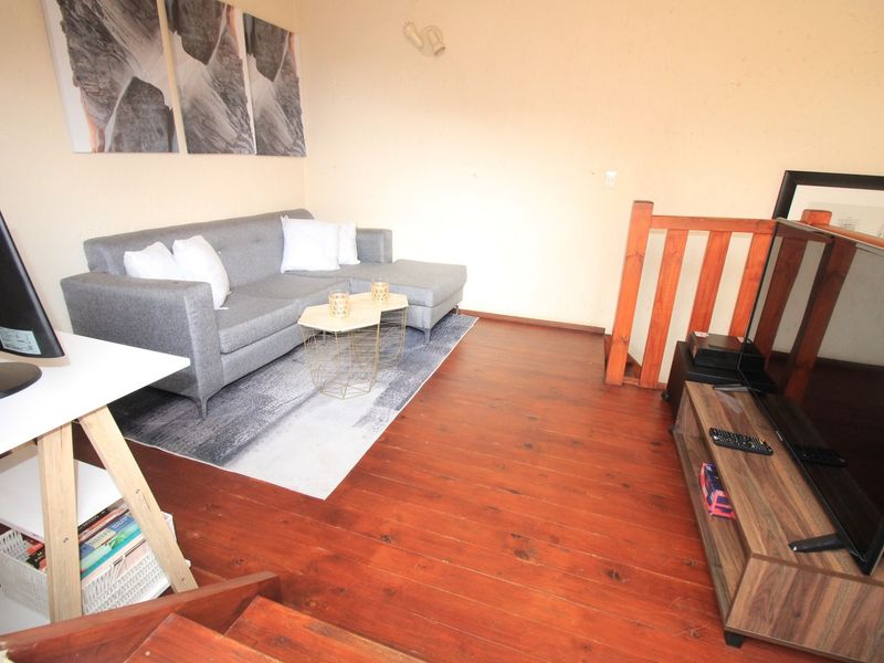 A living room area featuring warm-toned wooden flooring and a wooden staircase railing, providing a cozy and functional space.