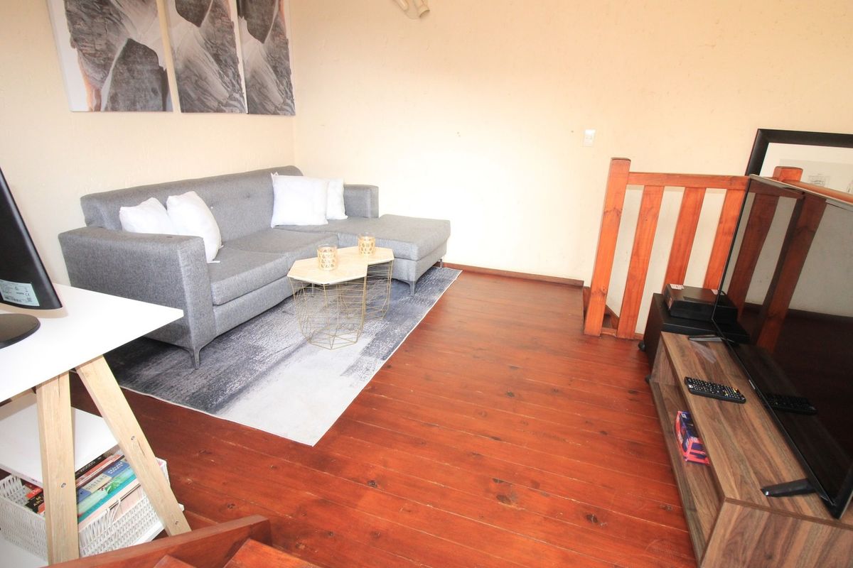 A living room area featuring warm-toned wooden flooring and a wooden staircase railing, providing a cozy and functional space.