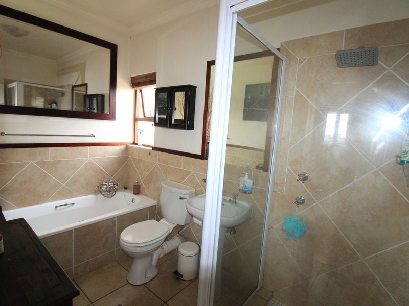 A functional bathroom featuring a bathtub, separate shower enclosure, pedestal basin, and toilet with neutral wall and floor tiling.
