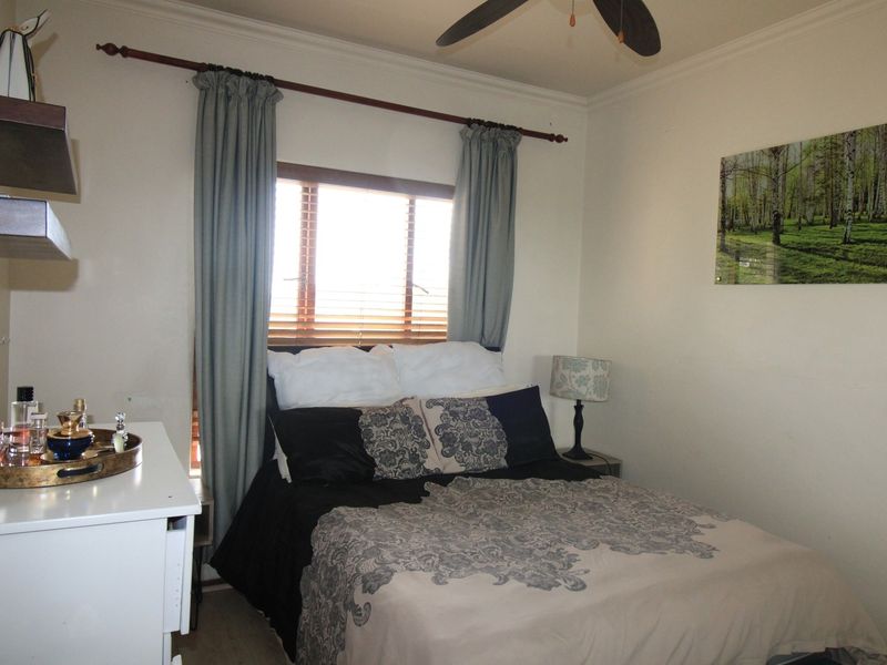 A cozy bedroom featuring a ceiling fan, wooden blinds, and crown molding, providing a comfortable and functional sleeping space.