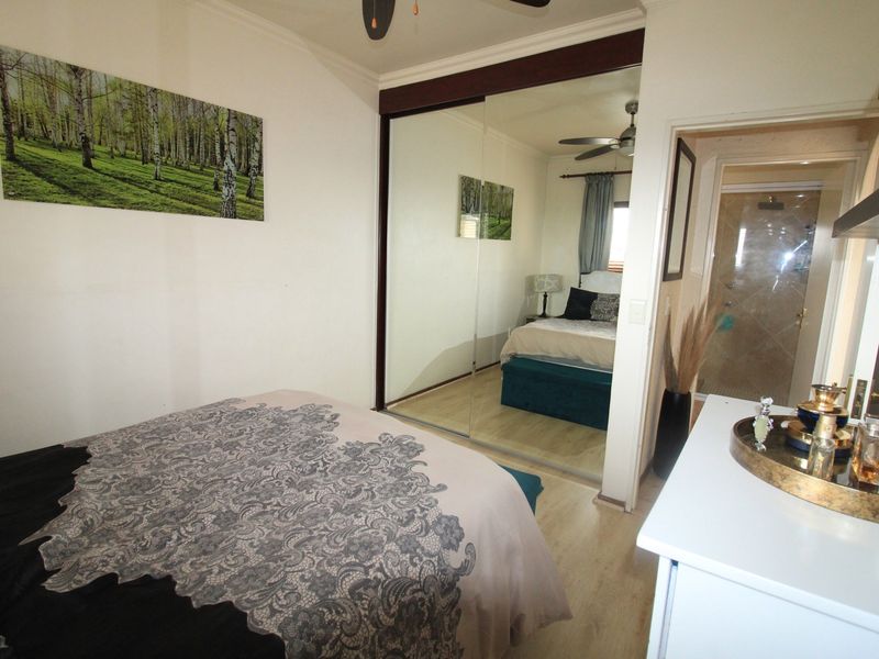 A well-maintained bedroom featuring laminate flooring, a large mirrored sliding wardrobe, and an integrated ceiling fan, with direct access to an en-suite bathroom.