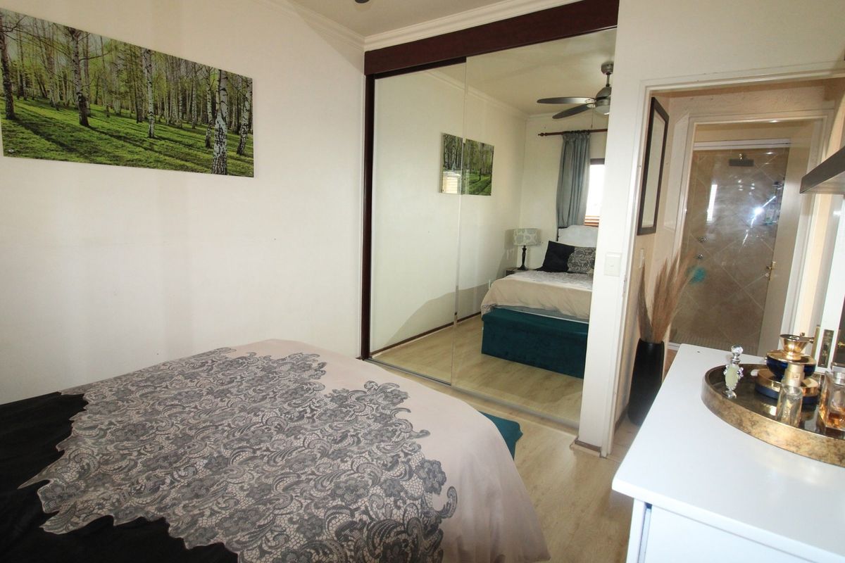 A well-maintained bedroom featuring laminate flooring, a large mirrored sliding wardrobe, and an integrated ceiling fan, with direct access to an en-suite bathroom.