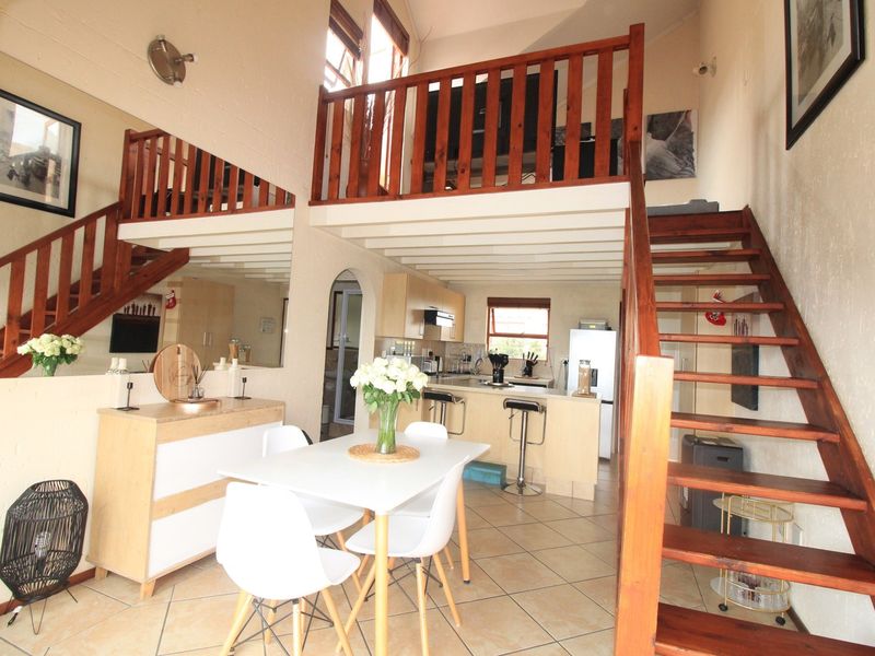 Open-plan living and kitchen area featuring a wooden staircase leading to a mezzanine level, tiled flooring, and functional built-in cabinetry.