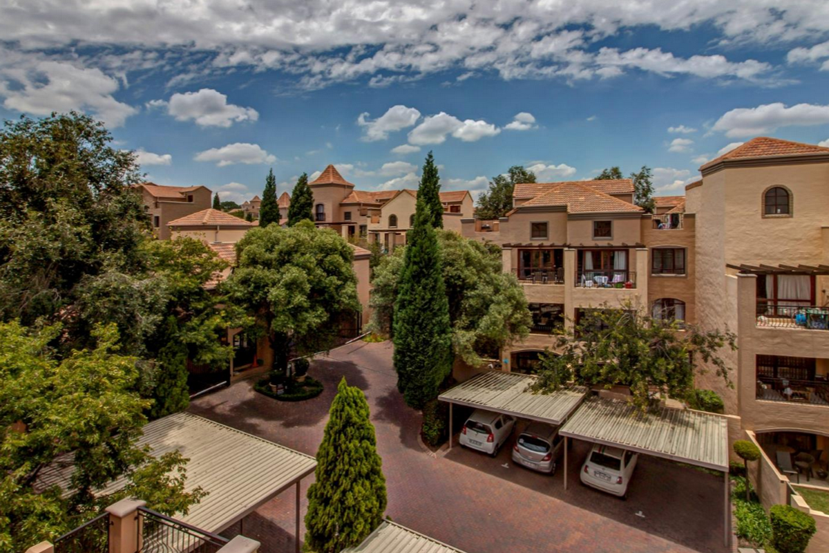 An elevated view of the apartment complex courtyard featuring paved driveways, covered parking carports, and established garden landscaping.