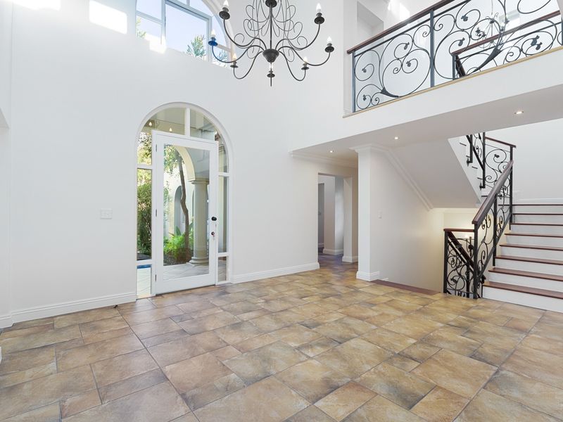 Spacious double-volume entrance hall featuring tiled flooring, an elegant wrought iron staircase, and an arched glass door providing natural light.