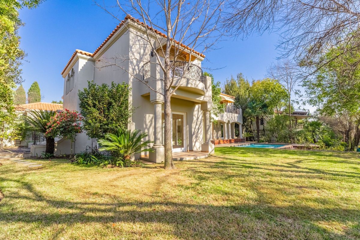 Rear view of the property featuring a landscaped garden, swimming pool, and a balcony with wrought iron railings and classic architectural columns.