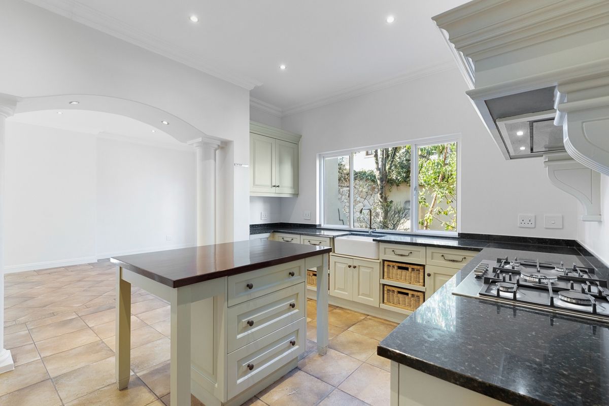 A bright, well-maintained kitchen featuring classic cabinetry, granite countertops, a gas hob, and a central island, complemented by tiled flooring and recessed lighting.