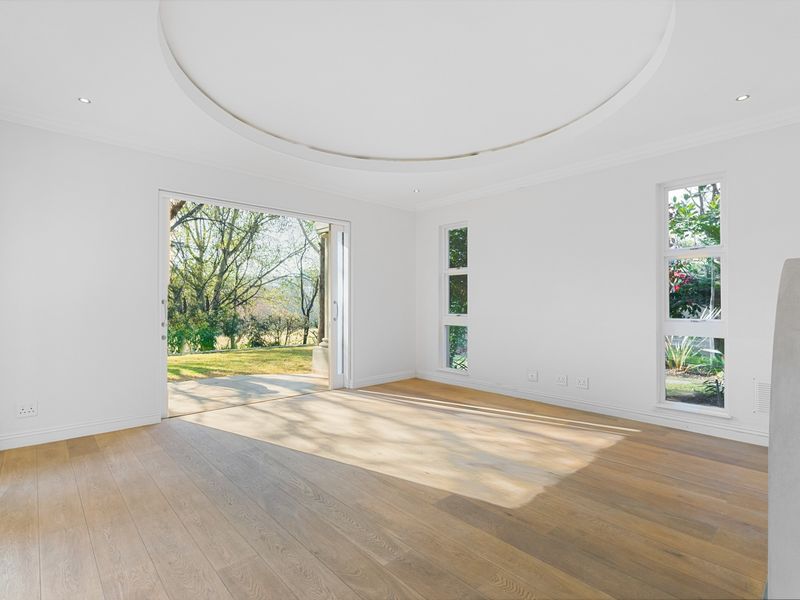 A bright, empty living room featuring hardwood flooring, a circular recessed ceiling detail, and large sliding doors opening to a garden view.