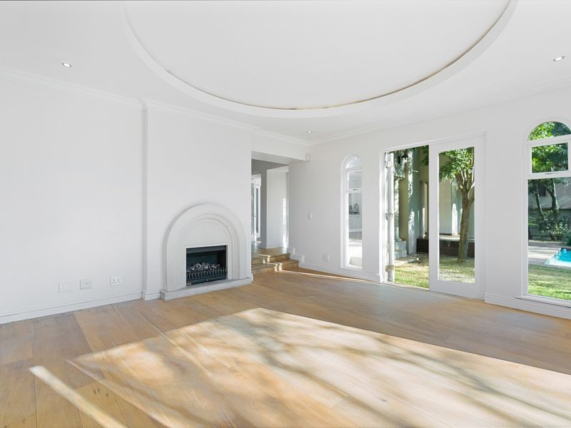Spacious living room featuring hardwood floors, a decorative gas fireplace, recessed ceiling detail, and arched glass doors opening to the garden.