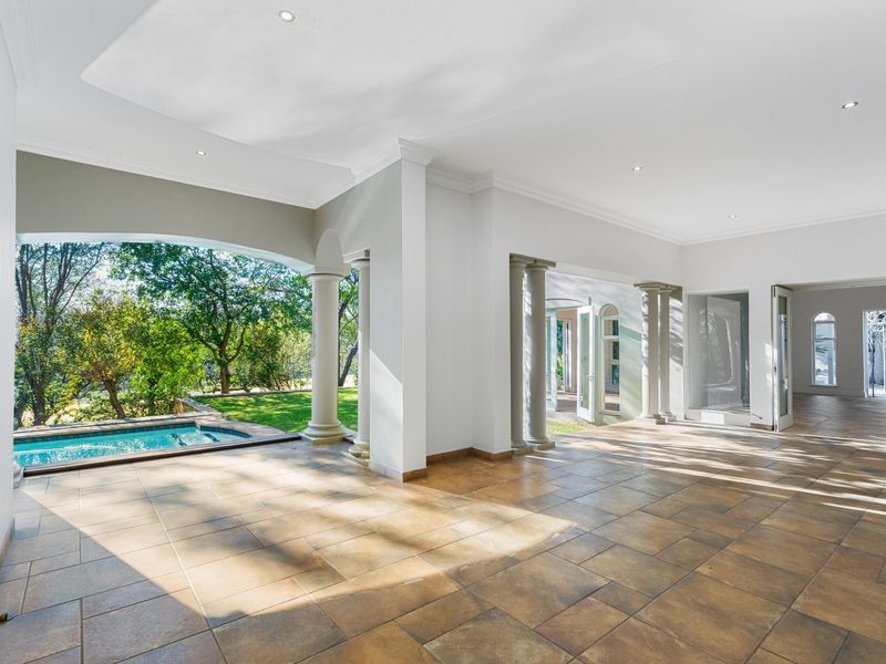 Spacious covered patio featuring tiled flooring, decorative columns, and direct access to the swimming pool and garden area.