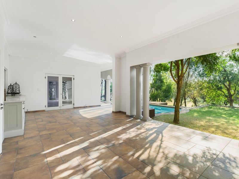 Spacious covered patio featuring tiled flooring, recessed lighting, and built-in cabinetry, offering seamless access to the garden and pool area.