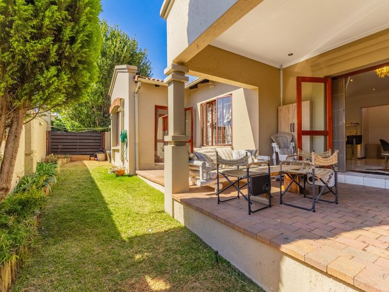 A covered brick-paved patio area overlooking a private garden, featuring structural pillars and direct access to the interior living space.