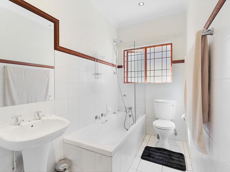 A functional bathroom featuring a pedestal basin, a bathtub with a shower mixer and glass screen, and a toilet, finished with white wall tiles.