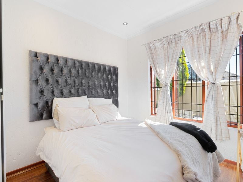 A bright bedroom featuring laminate flooring, recessed downlighting, and a window fitted with security bars.