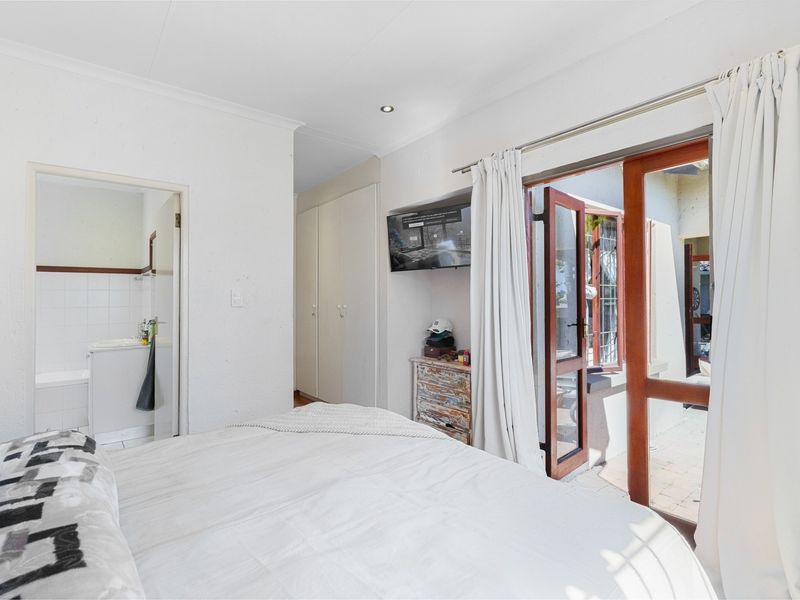A bedroom featuring built-in cupboards, recessed lighting, and direct access to an en-suite bathroom and an outdoor patio area through wooden doors.