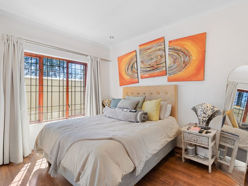 A well-lit bedroom featuring laminated flooring, recessed downlighting, and security bars on the window, providing a comfortable and secure living space.