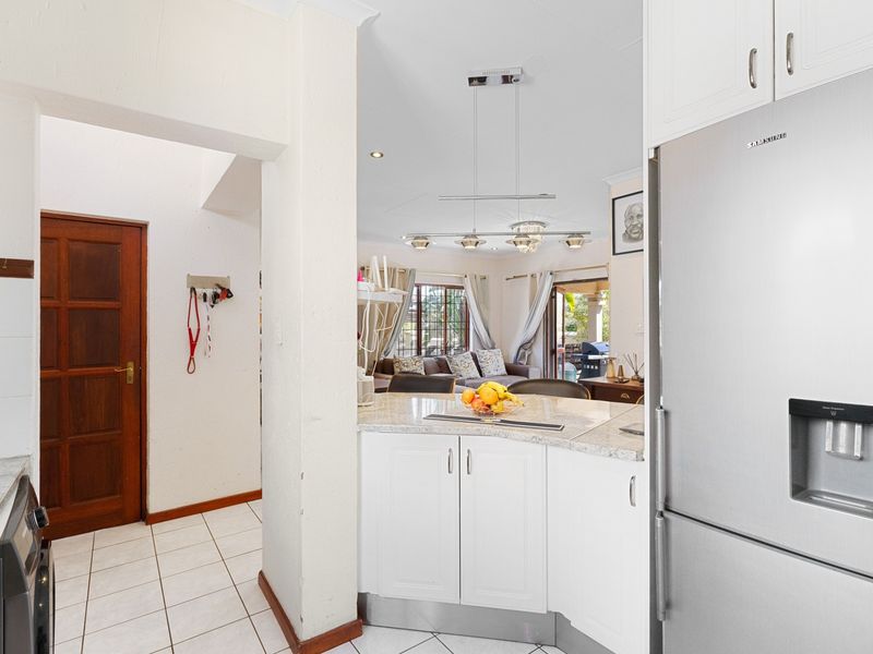 Open-plan kitchen area featuring white cabinetry, granite countertops, and tiled flooring, flowing into a bright living space with access to an outdoor patio.