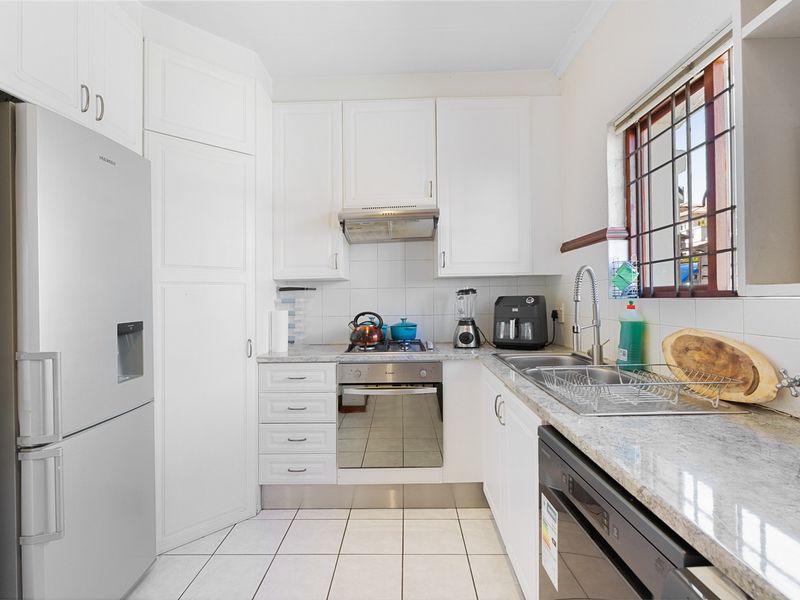 A functional kitchen featuring white cabinetry, granite countertops, built-in oven, hob, extractor fan, and tiled flooring with a window providing natural light.