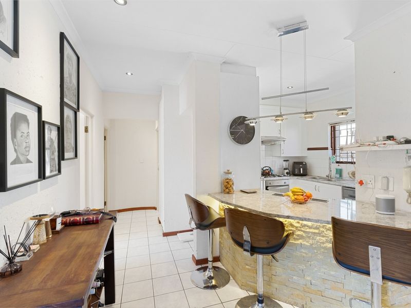 Open-plan kitchen and living area featuring a stone-clad breakfast bar, granite countertops, modern pendant lighting, and tiled flooring throughout.