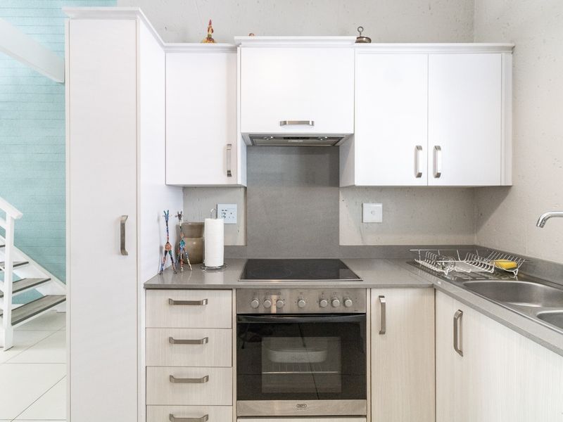 Compact modern kitchen featuring white cabinetry, stone countertops, integrated electric hob and oven, and a stainless steel sink.