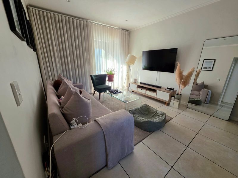 A bright and well-maintained living room featuring large format floor tiles, recessed lighting, and a sliding glass door with floor-to-ceiling curtains.