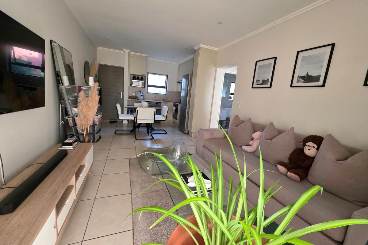 An open-plan living and kitchen area featuring neutral tiled flooring, recessed lighting, and a functional kitchen layout with built-in cabinetry and appliances.