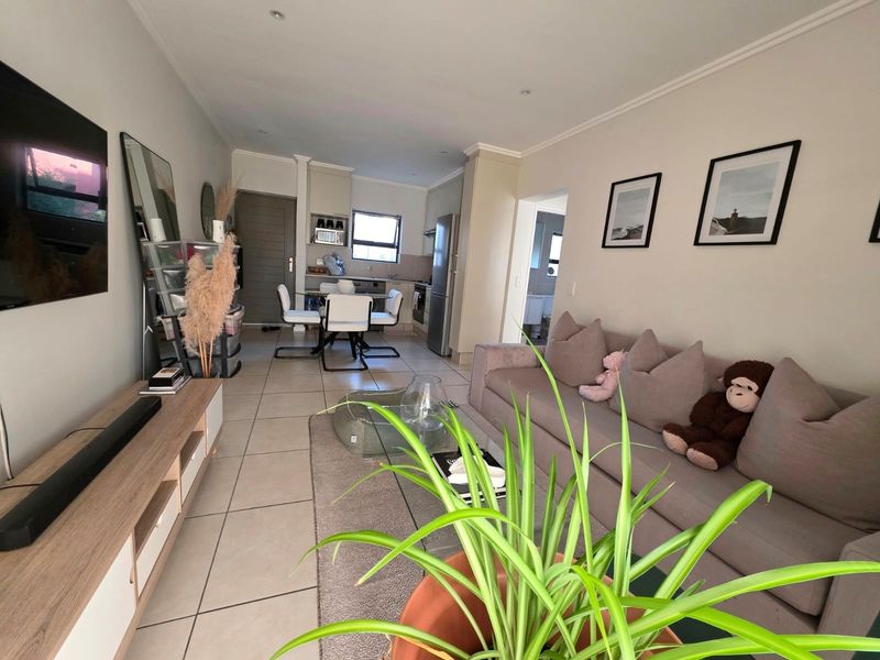An open-plan living and kitchen area featuring neutral tiled flooring, recessed lighting, and a functional kitchen layout with built-in cabinetry and appliances.